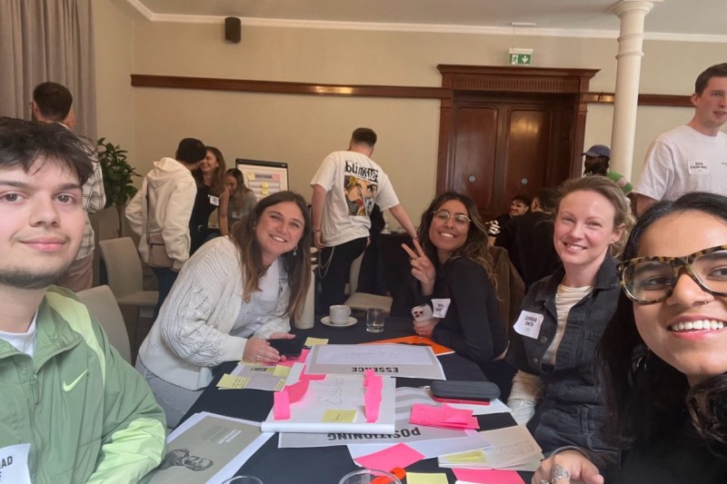 A selfie style photo of students around a table with flip charts and post-it notes