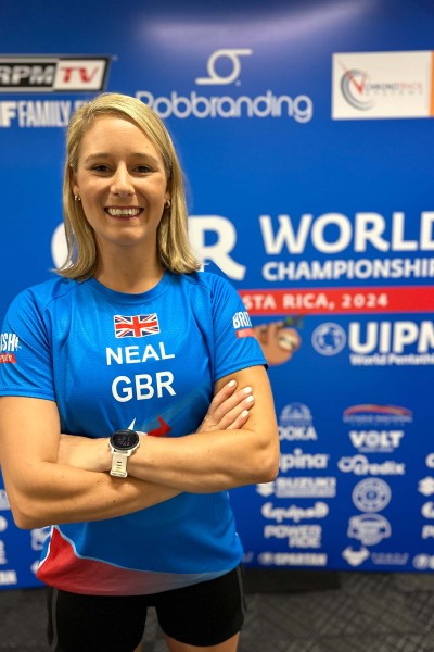 Becky wearing her British Team T-Shirt in front of a banner for the World Obstacle Course Championships