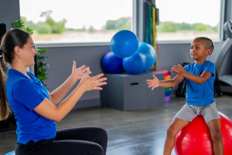 A woman and child on balance balls throwing a ball between them