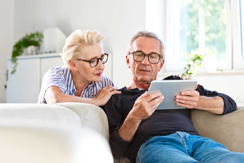 An older man and woman on a sofa looking at a tablet device