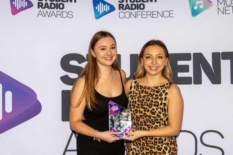 Hannah and Kitty holding their award, looking at the camera smiling