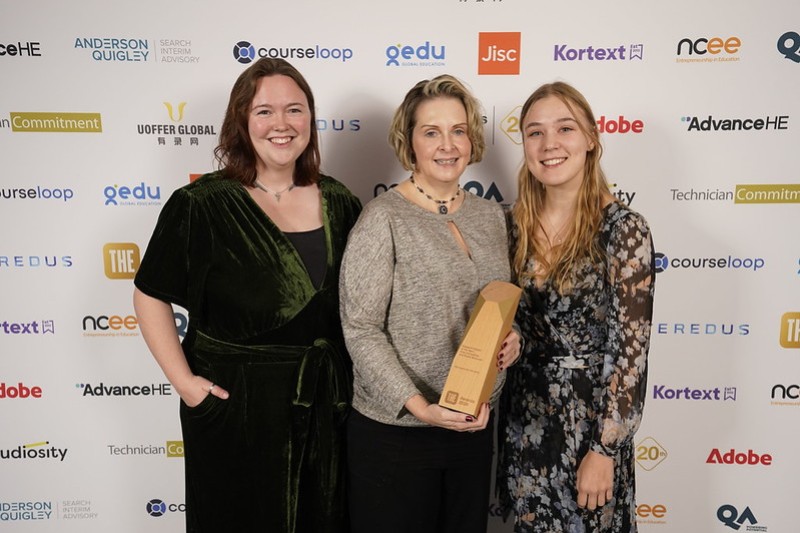 The women standing looking at the camera smiling, the lady in the centre holding their award