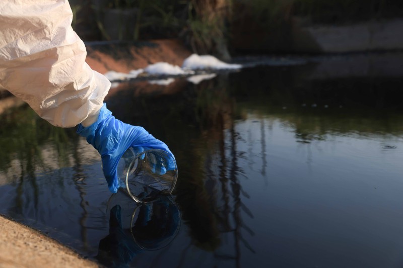 A gloved hand gathering a water sample into a glass beaker