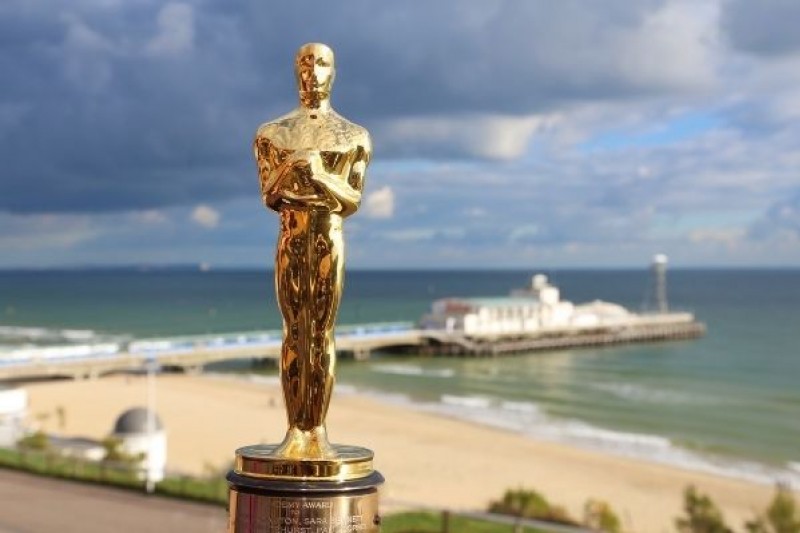 An Oscar statue, with Bournemouth beach and pier in the background