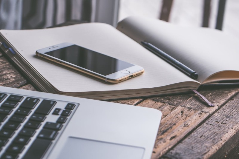 A laptop positioned next to a notepad with a phone on it